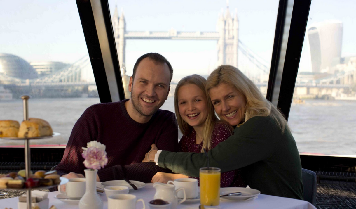 A family of three have afternoon tea on board City Cruises in front of Tower Bridge